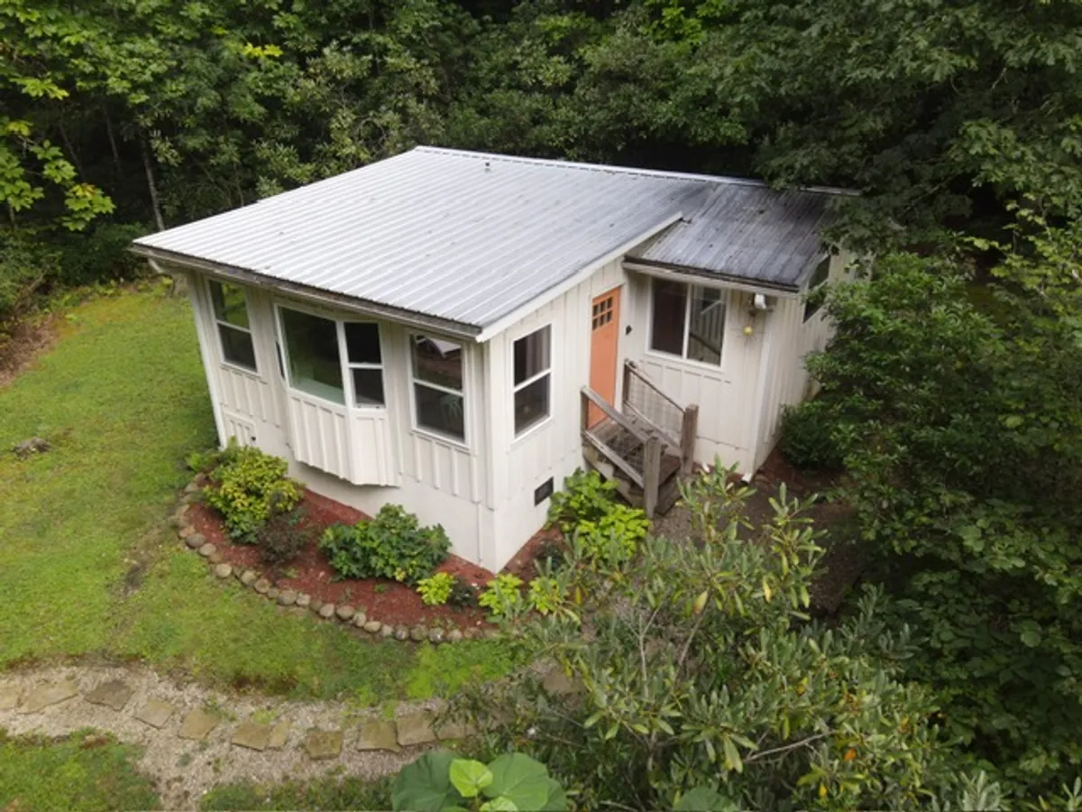 A charming exterior shot of the cottage, showing the house, its pathway, and surrounding greenery. The scene suggests opportunities for relaxation on the porch, with the landscape inviting guests to enjoy the outdoors or prepare for nearby adventures.